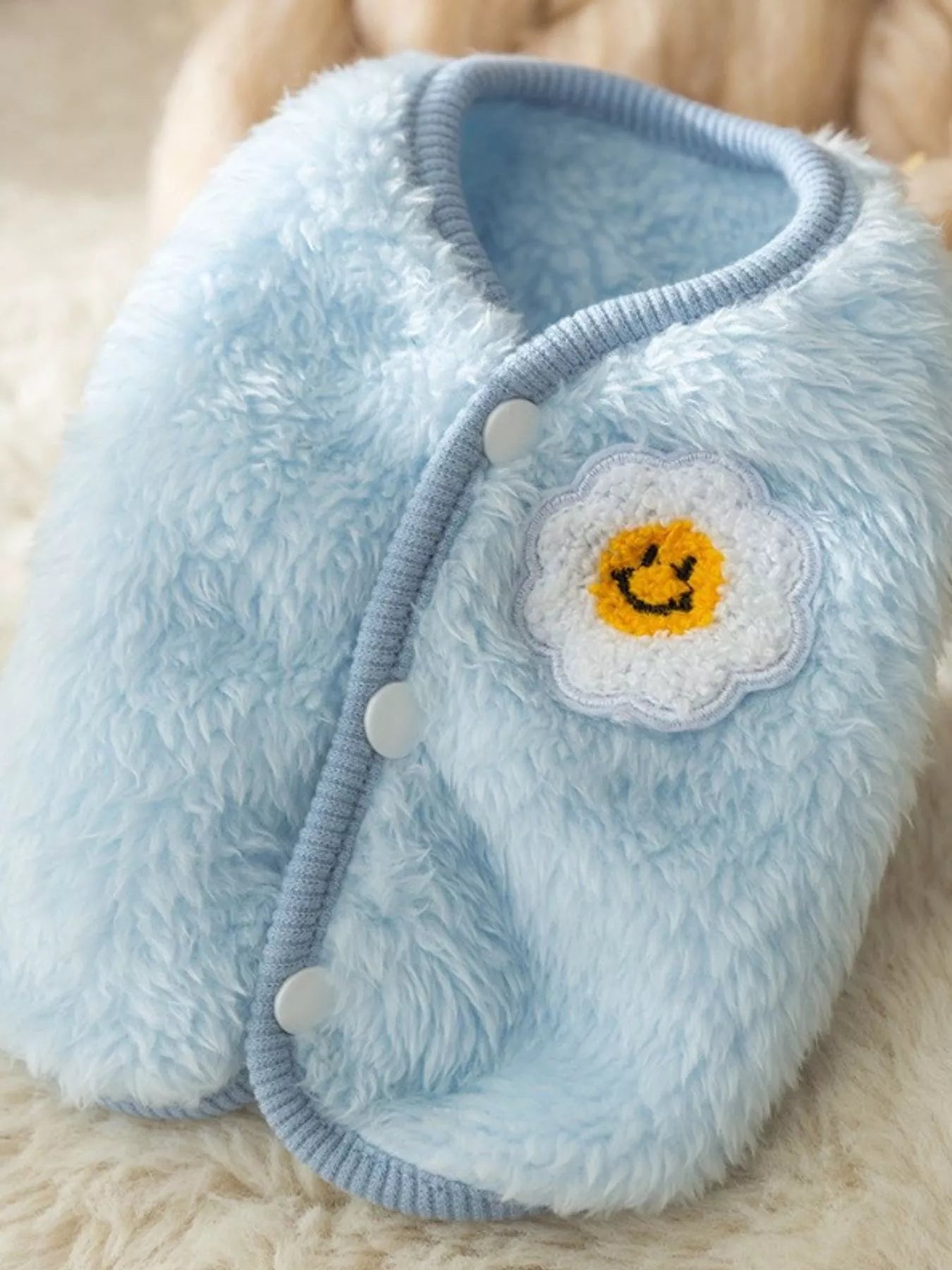 Blue fuzzy eye mask with a flower design on a beige background