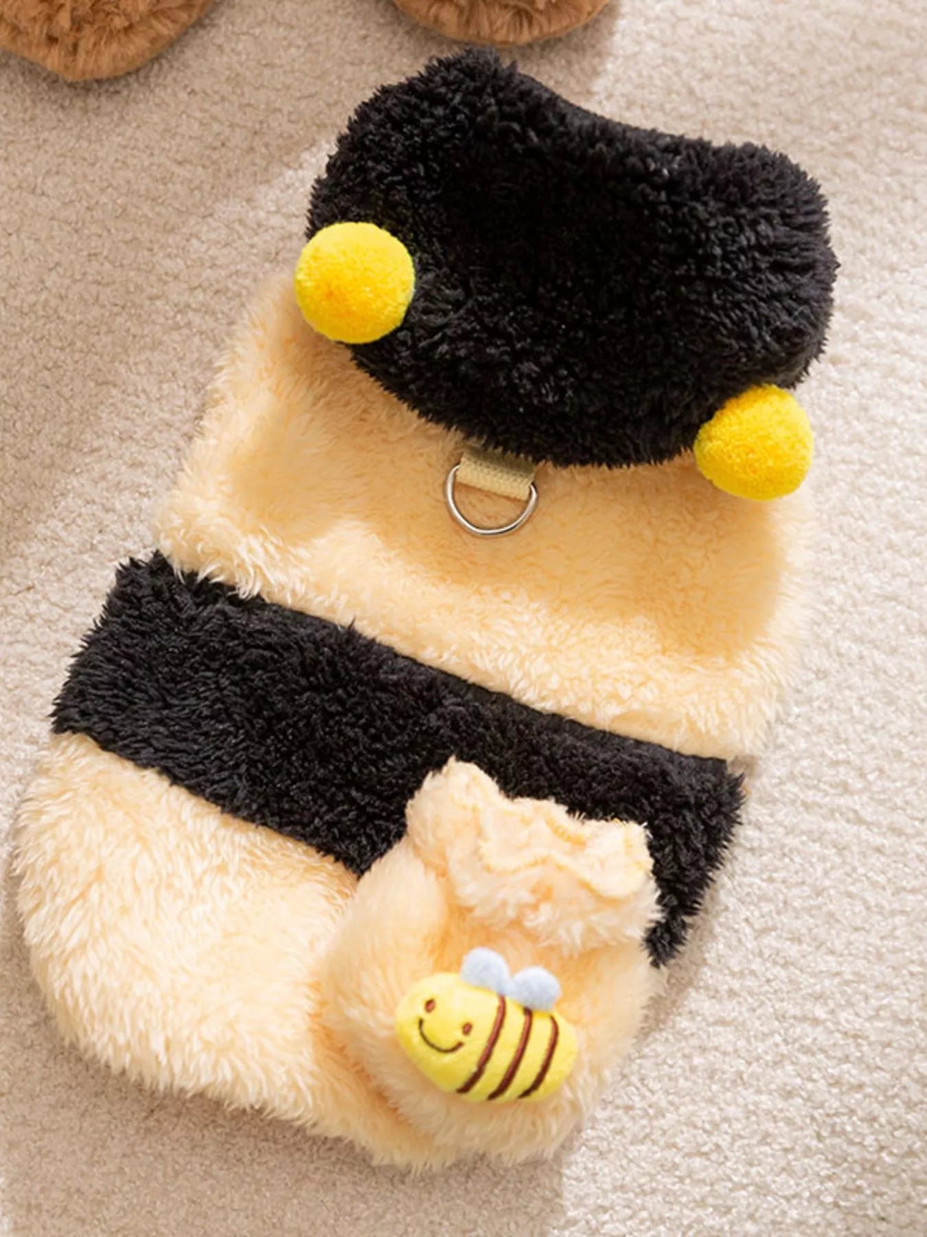 Plush toy bee with a fuzzy black and yellow striped body on a beige surface