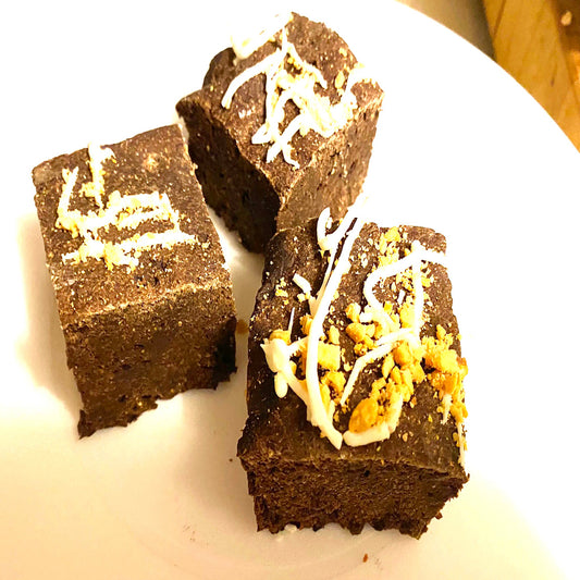 Three chocolate brownies with white drizzle and orange bits on a white plate.