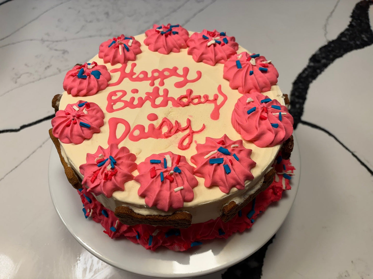 Birthday cake with pink frosting and 'Happy Birthday Daisy' text on a white plate.