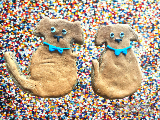 Two dog-shaped cookies with blue collars on a colorful sprinkles background