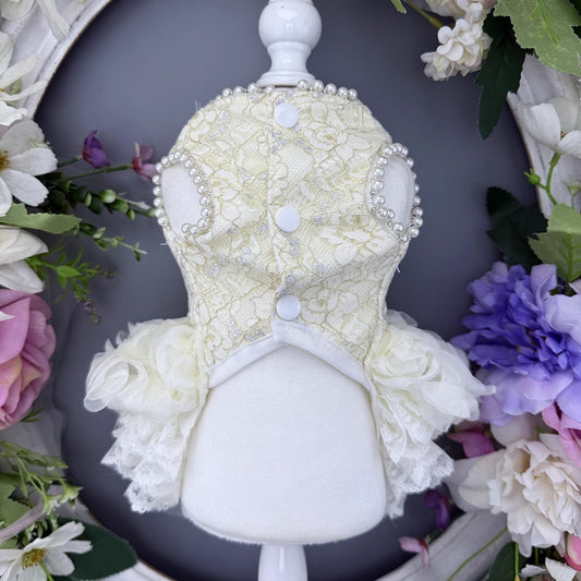 Decorative headpiece with lace and pearls on a mannequin head, surrounded by flowers.
