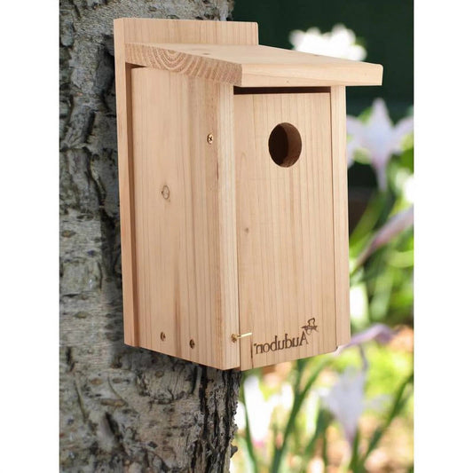 Wooden birdhouse attached to a tree trunk with a blurred natural background