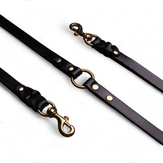 Black leather dog leashes with gold hardware on a white background