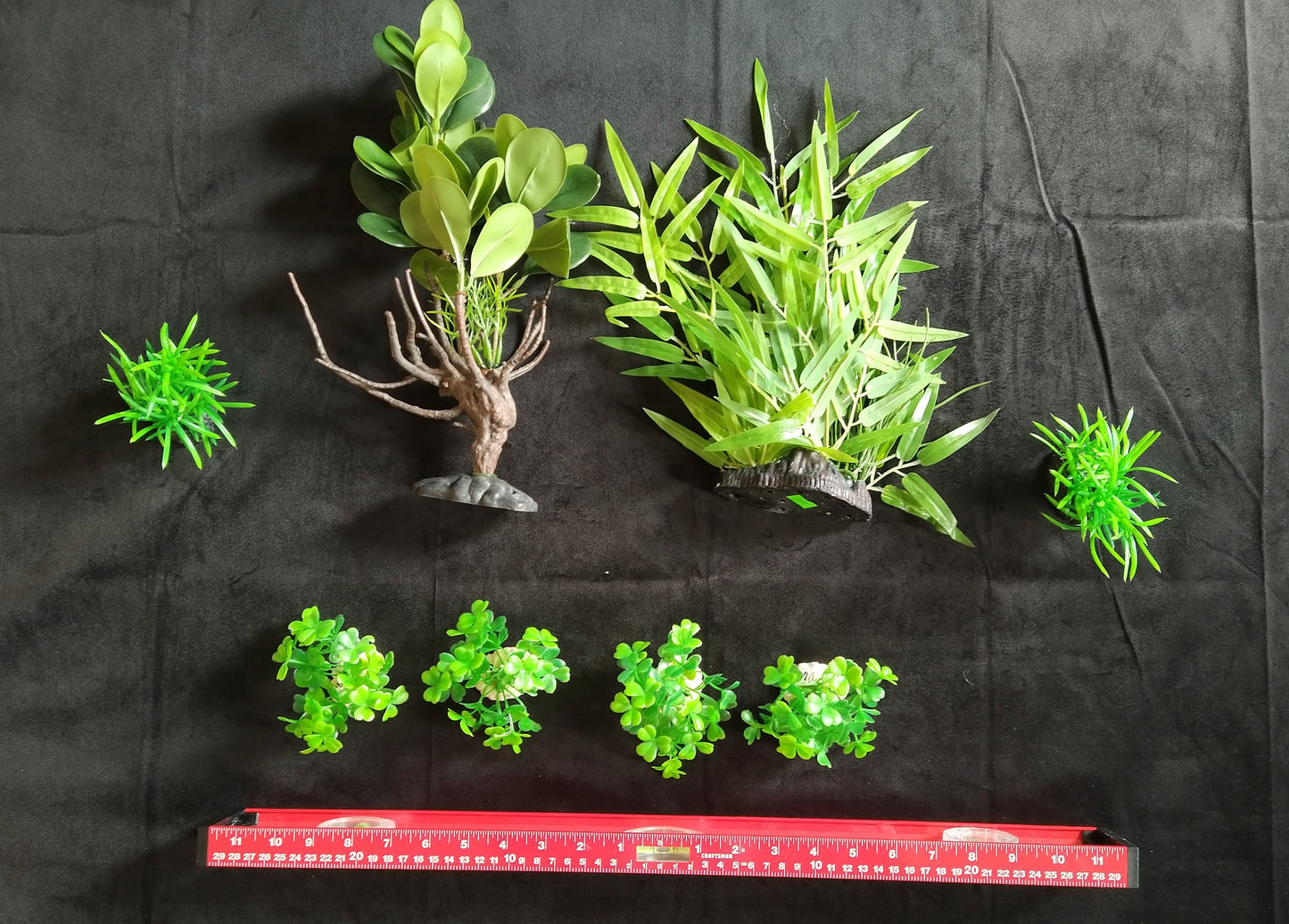 Set of green artificial plants on a black background with a red ruler for scale.
