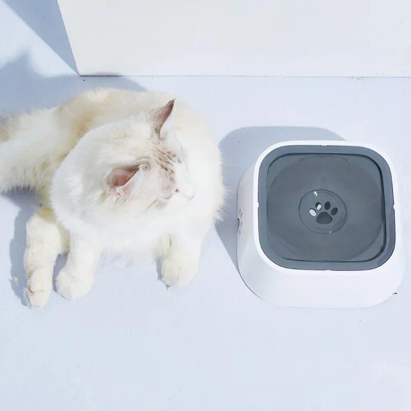 Cat lying next to a square pet water fountain on a white surface.