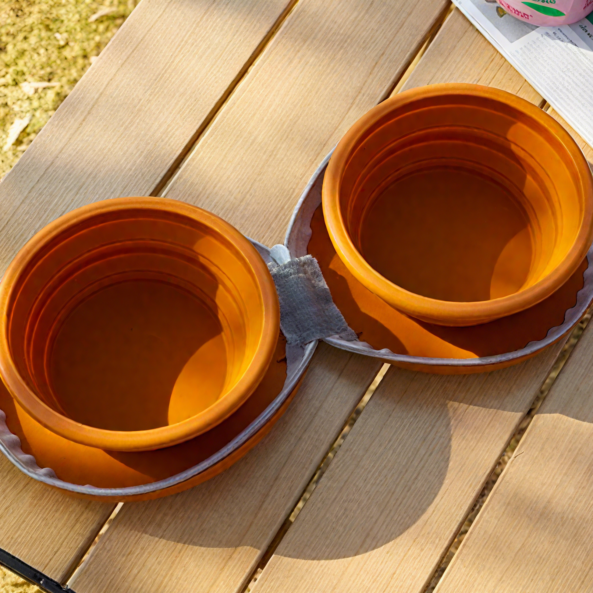 Two orange collapsible bowls on a wooden surface outdoors.