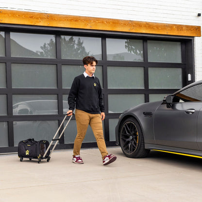 Person with a suitcase walking next to a gray car in front of a modern garage door.