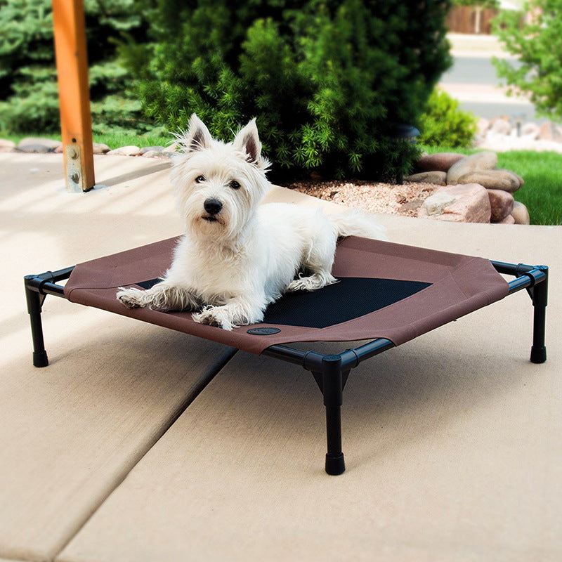 Dog lying on a brown pet cot outdoors with greenery in the background