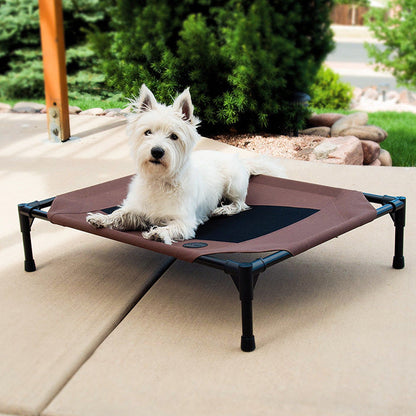 Dog lying on a brown pet cot outdoors with greenery in the background