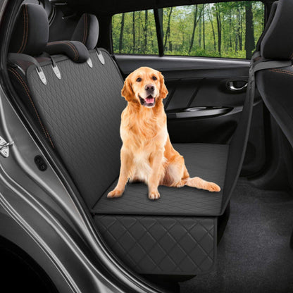 Dog sitting on a black car seat cover inside a vehicle with a forest view outside.