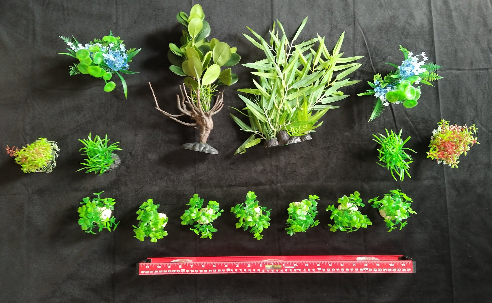 Collection of green artificial plants on a black background with a ruler for scale.
