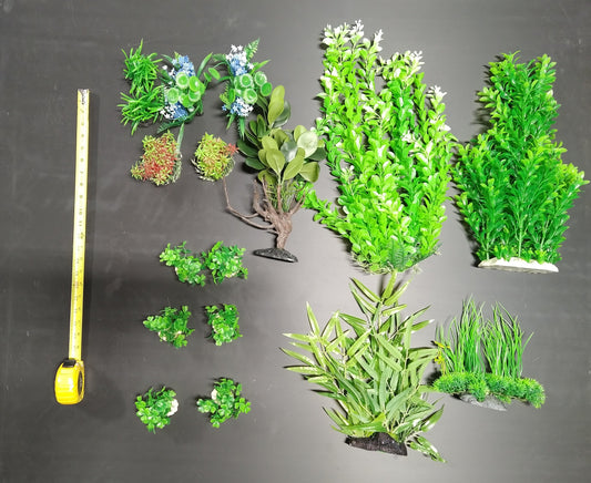 Assorted artificial green plants on a gray background with a tape measure for scale.