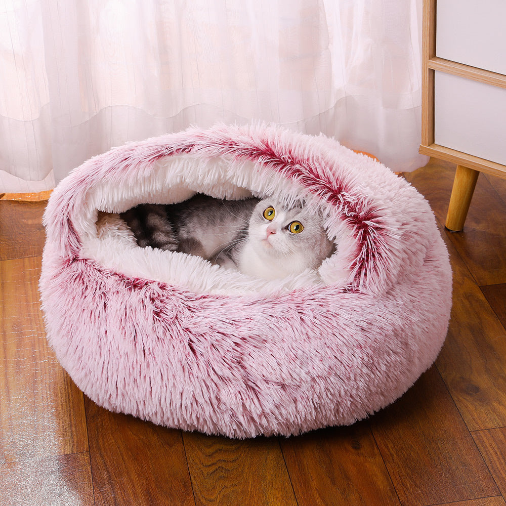 Cat inside a fluffy pink pet bed on a wooden floor with white curtains in the background