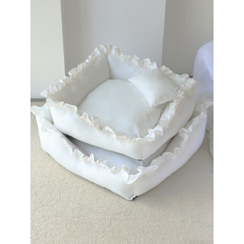 Stack of white pet beds with ruffled edges on a light surface.