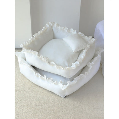 Stack of white pet beds with ruffled edges on a light surface.