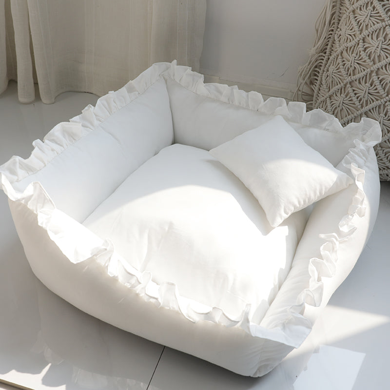 White pet bed with ruffled edges on a light-colored floor.