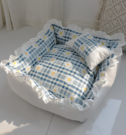 Pet bed with blue checkered pattern and white ruffles on a white surface.