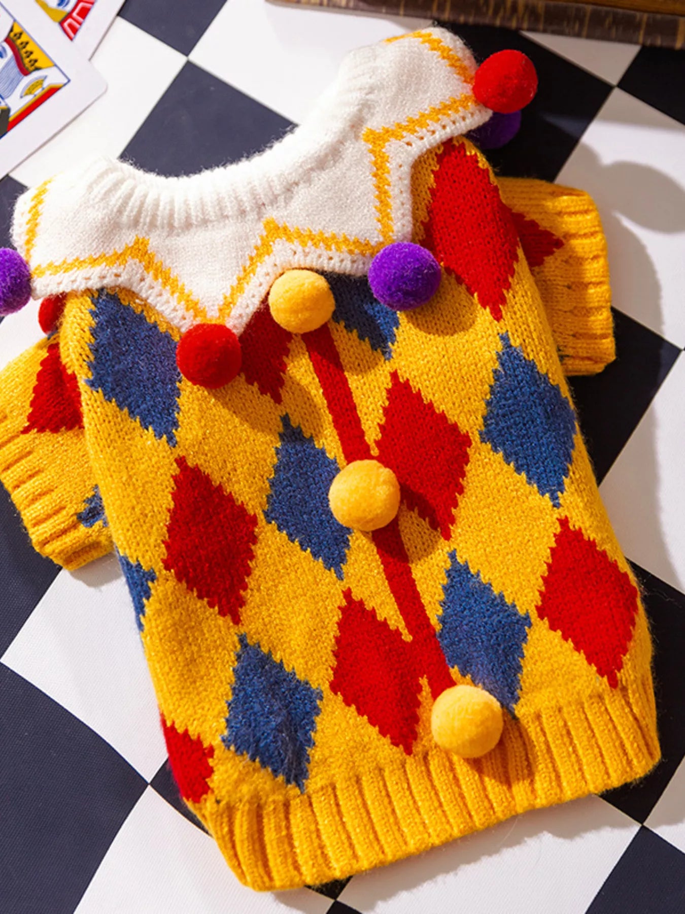 Colorful knitted sweater with diamond pattern and pom-poms on a checkered background