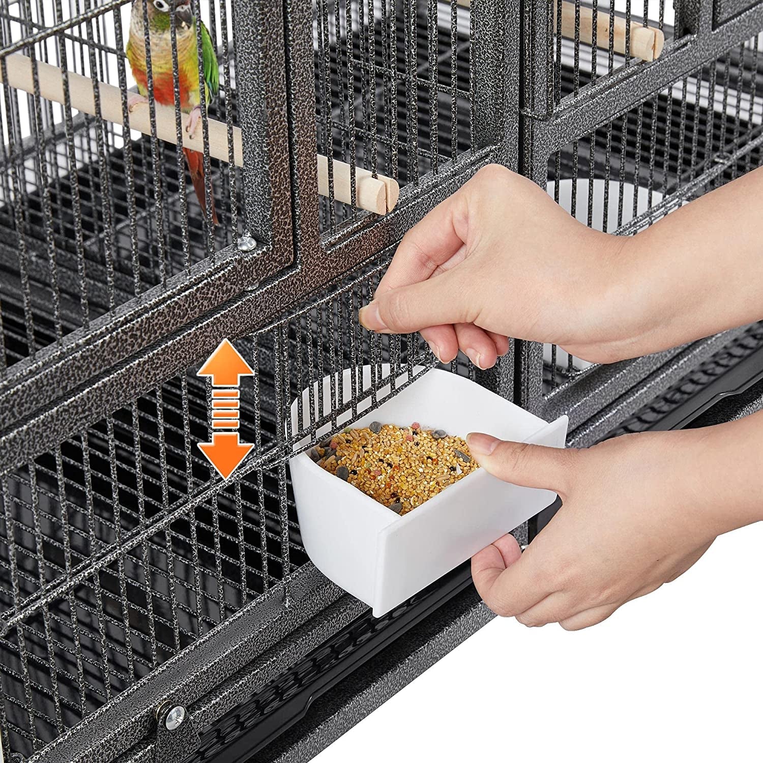 Person feeding a bird in a cage with a white dish containing bird food.