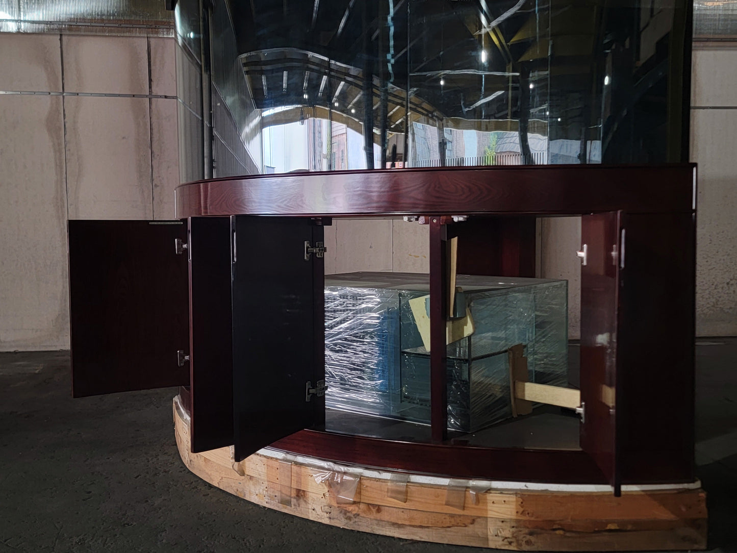 Curved wooden reception desk with glass panels in a room with tiled walls.