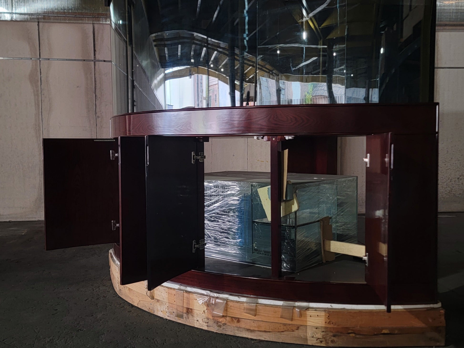 Curved wooden reception desk with glass panels in a room with tiled walls.