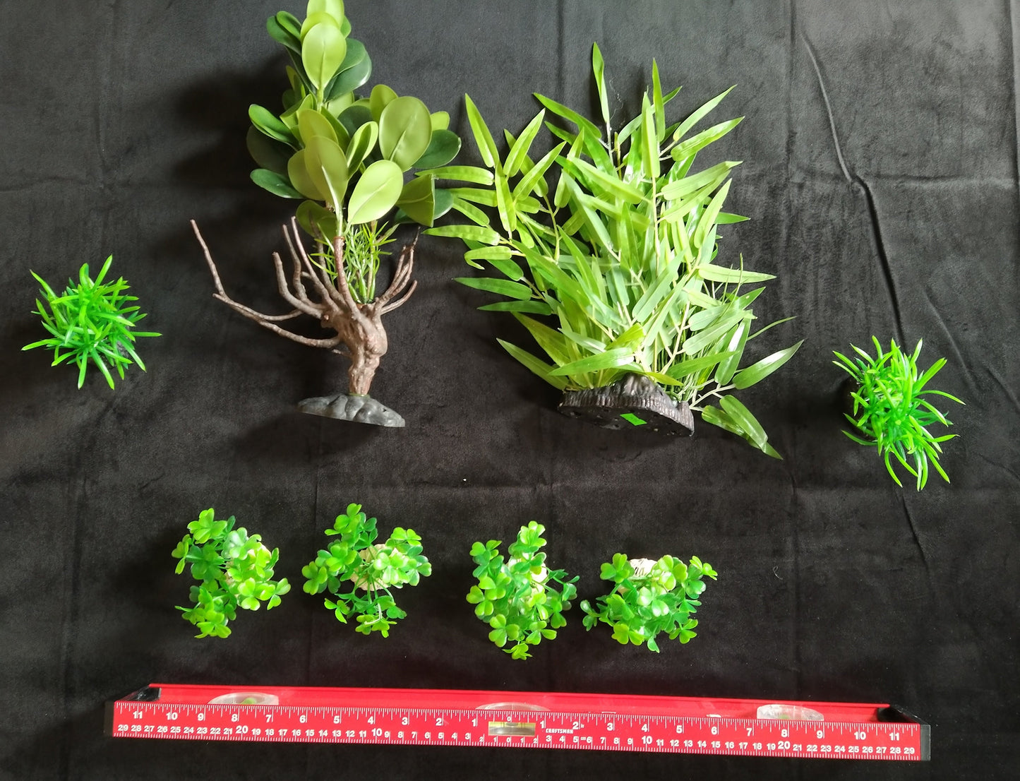 Set of green artificial plants on a black background with a red ruler for scale.