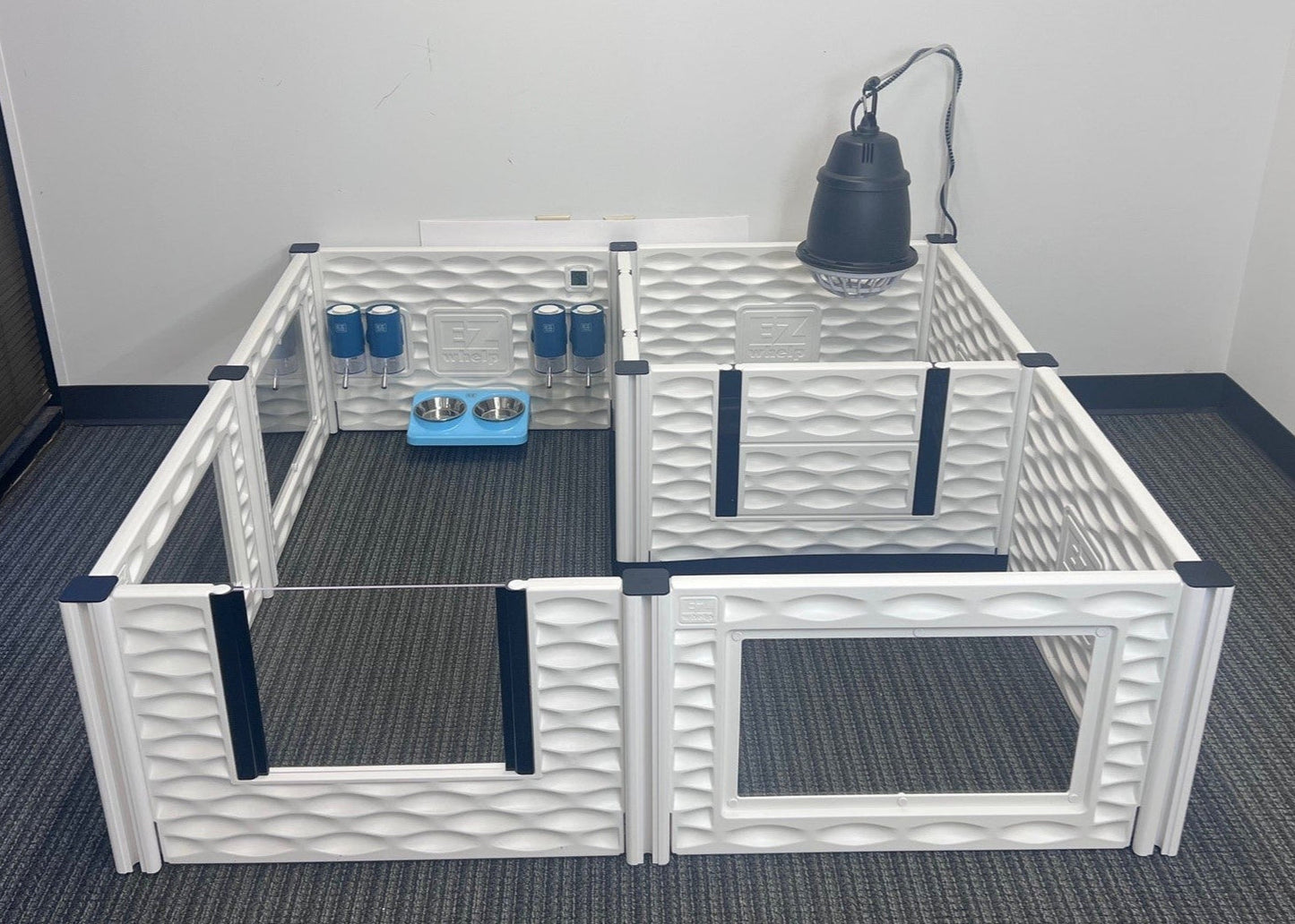 Pet playpen with water bowls and a lamp inside on a carpeted floor.