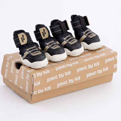 Four black and white pet boots on a branded cardboard box with 'paws by kai' text.