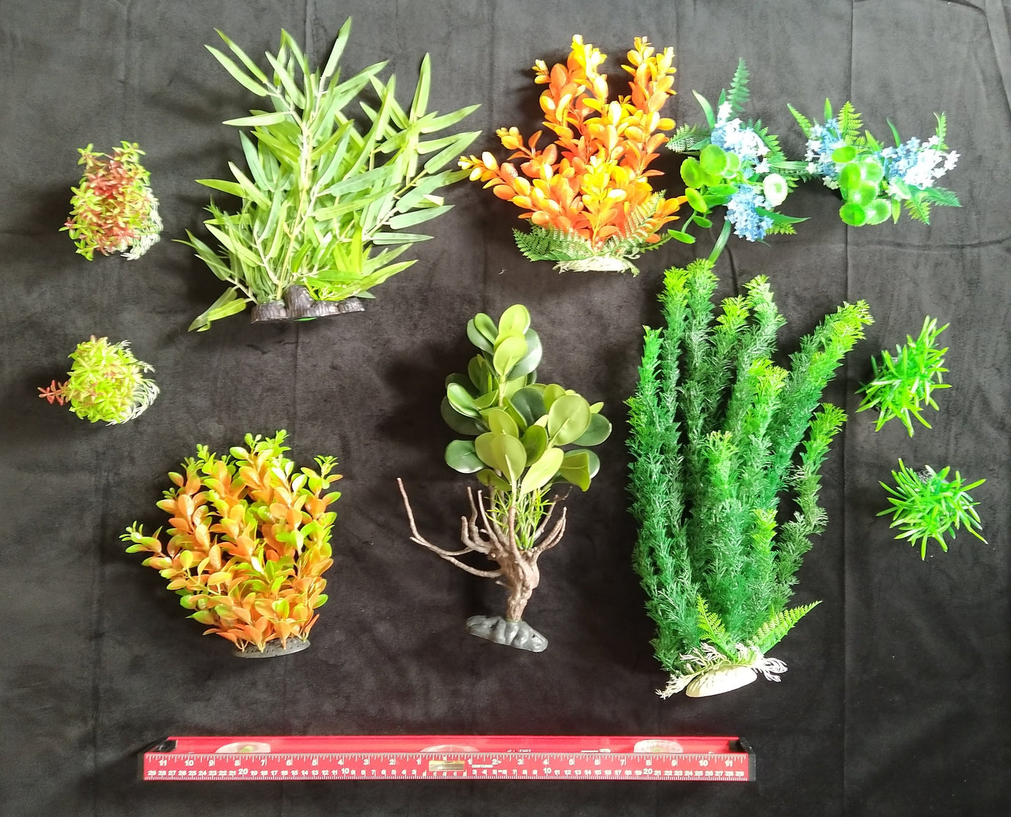 Collection of various artificial plants on a black background with a ruler for scale.