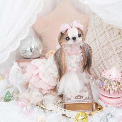 Small dog in a decorative outfit with a pink bow, surrounded by festive decorations.