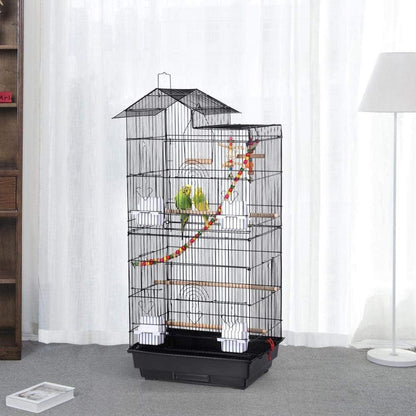 Bird cage with perches and toys inside, placed on a gray floor with white curtains in the background.