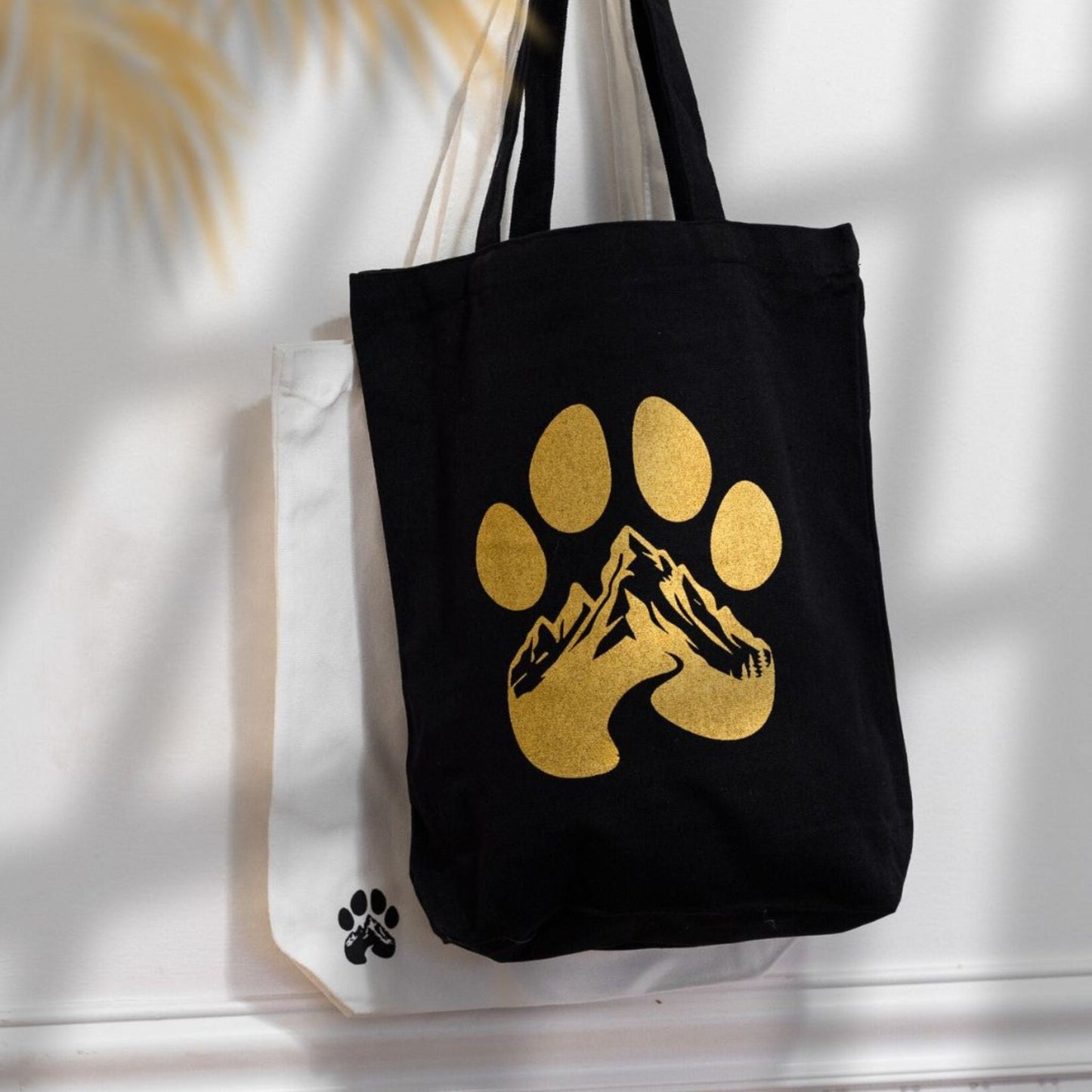 Black tote bag with gold paw print design on a white surface