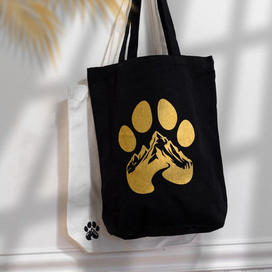 Black tote bag with gold paw print design on a white surface