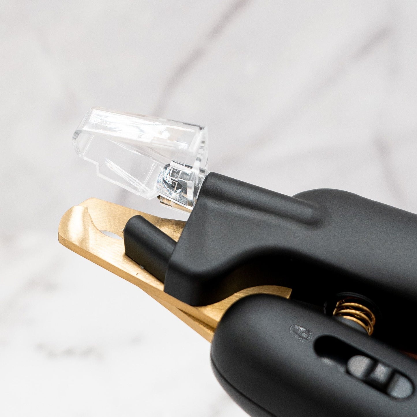 Black and gold tool with clear component on a light gray background