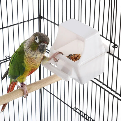 Bird perched on a branch next to a white geometric bird feeder in a cage.