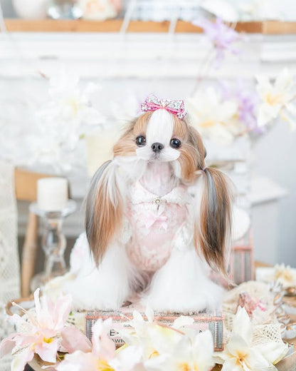 Dog with a bow on its head sitting on a table with flowers