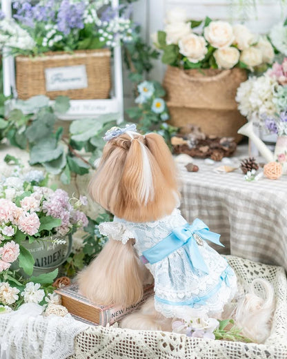 Small doll with blonde hair and a blue bow in a decorative setting with flowers and plants.