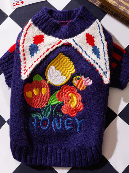 Children's sweater with embroidered design of a beehive, flowers, and the word 'Honey' on a checkered background.