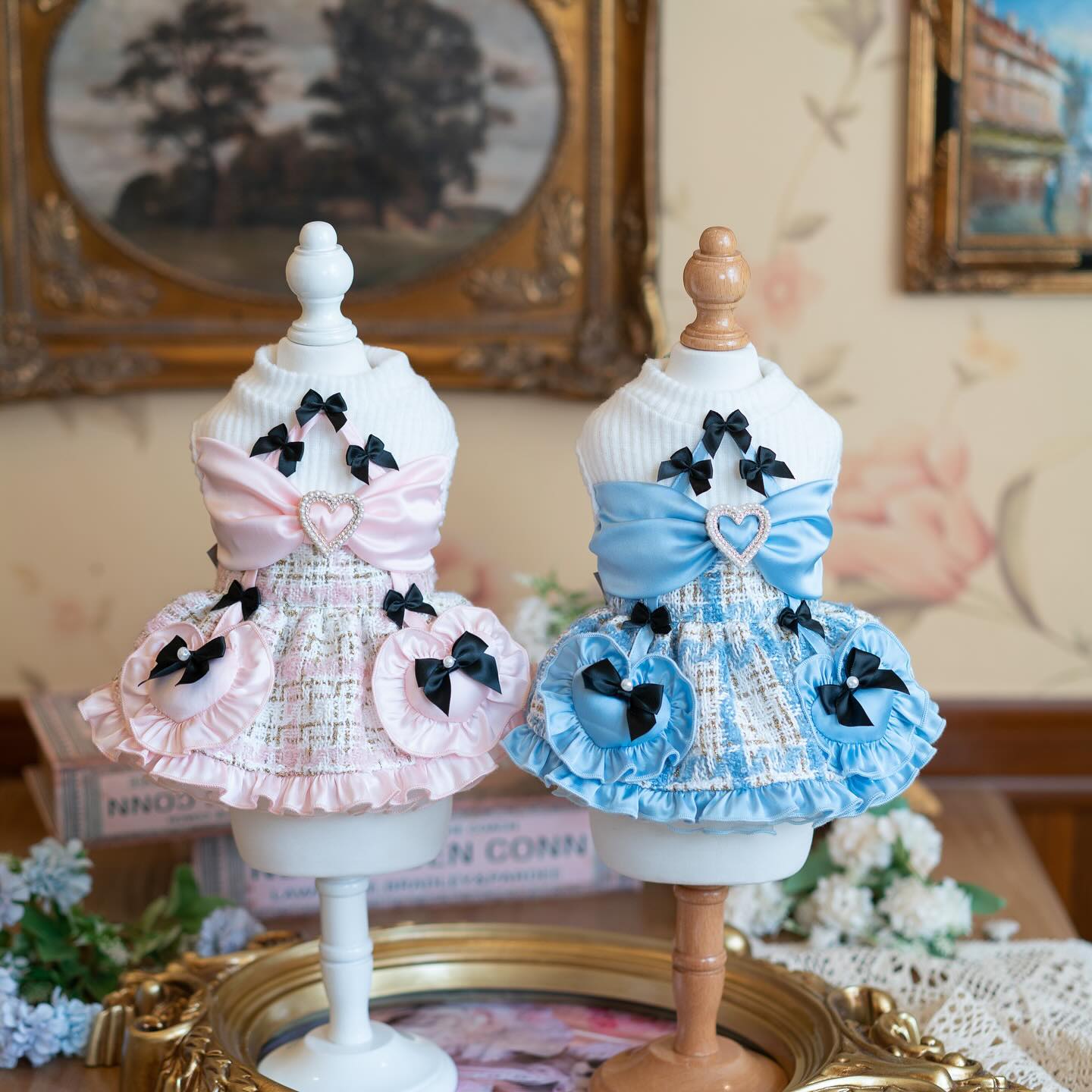 Two mannequins dressed in pink and blue checkered dresses with black bows on a decorative stand.