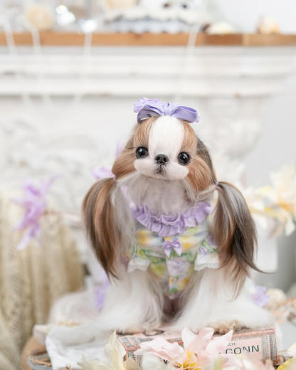 Small dog with pigtails wearing a floral outfit and purple bow in a decorative setting.