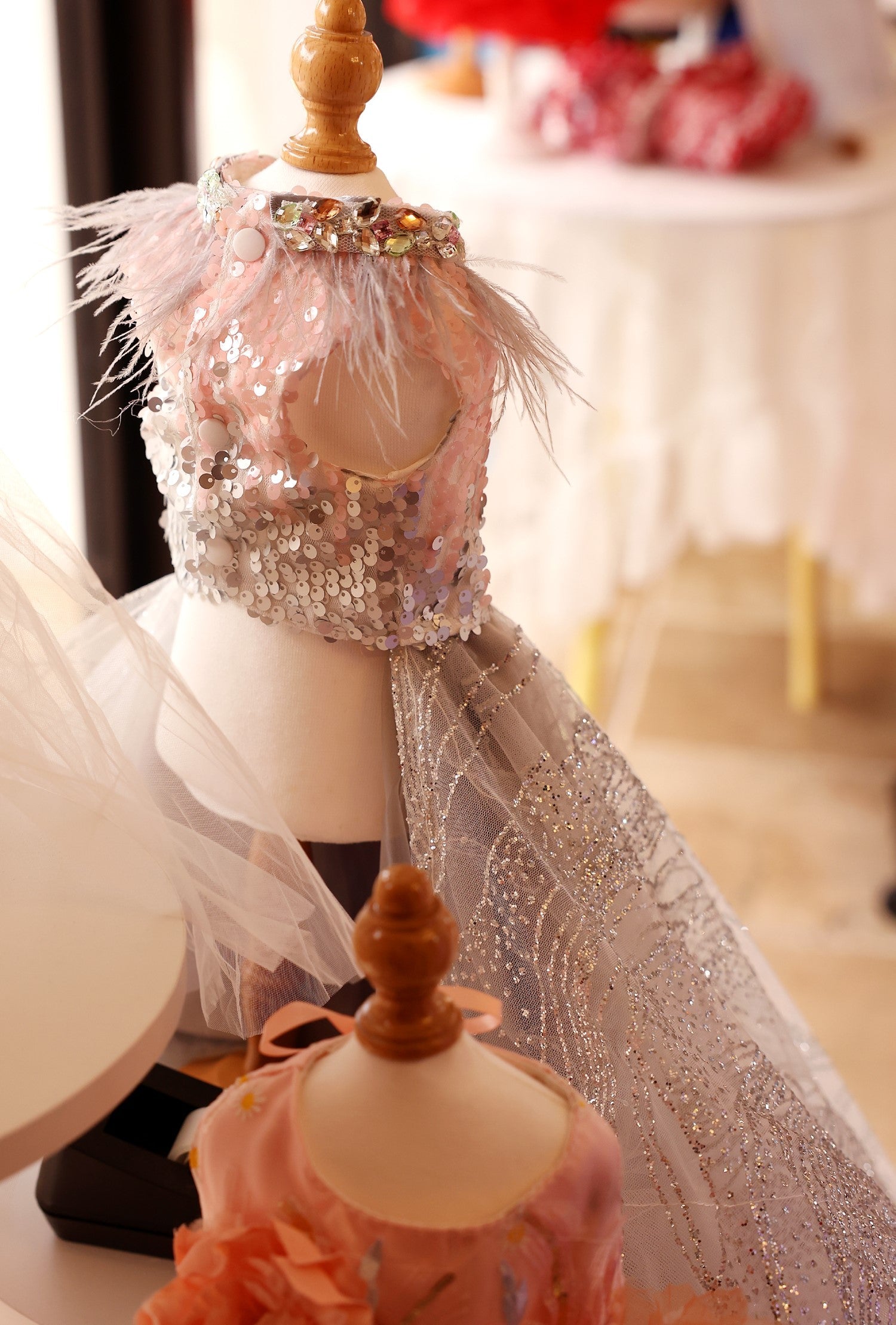 Decorative mannequin with a pink dress and feather details on a blurred indoor background