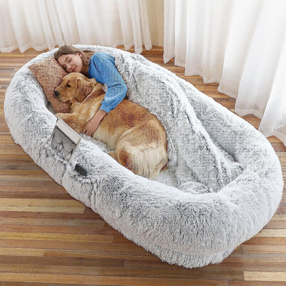 Woman hugging a dog in a fluffy pet bed on a wooden floor.