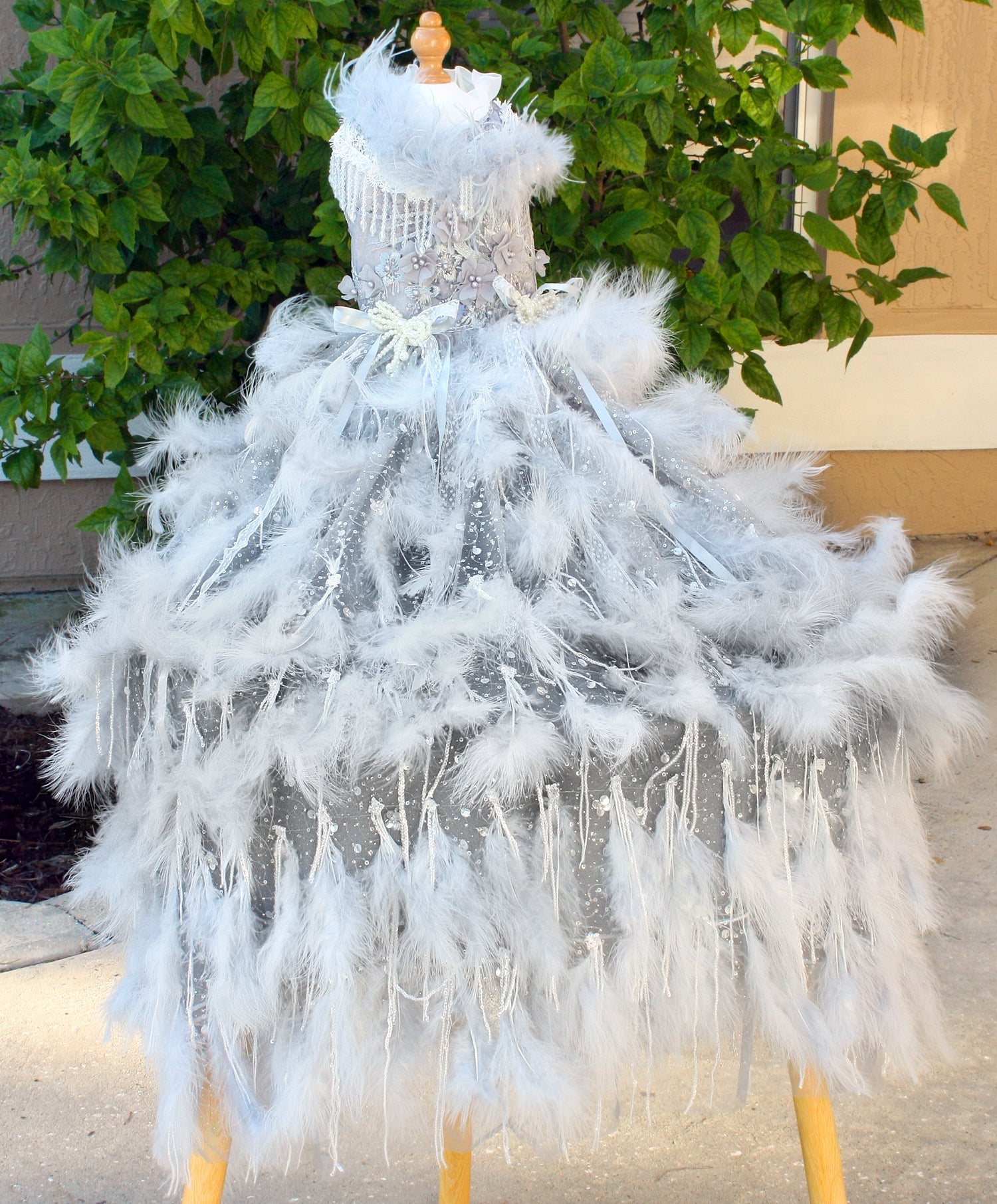 White feathered dress on a mannequin against a green leafy background