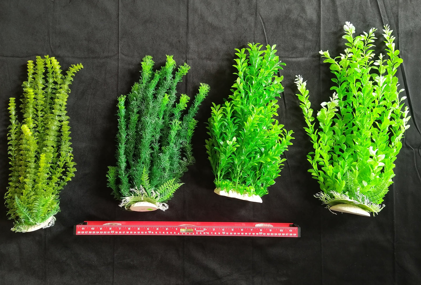 Four artificial plants of varying sizes on a black background with a ruler for scale.