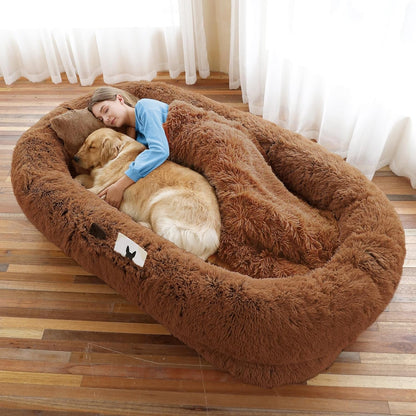 Woman and dog lying in a large brown fluffy pet bed on a wooden floor.