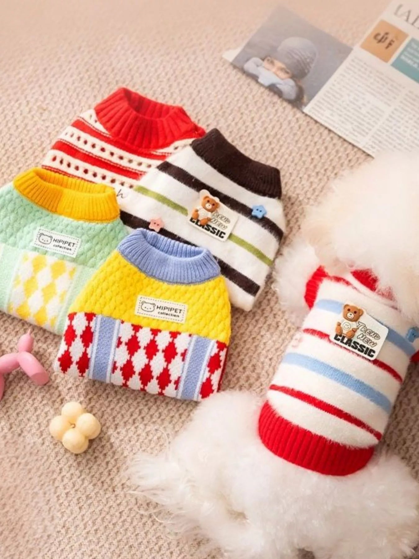 Colorful dog sweaters on a textured surface with a small toy and fur.
