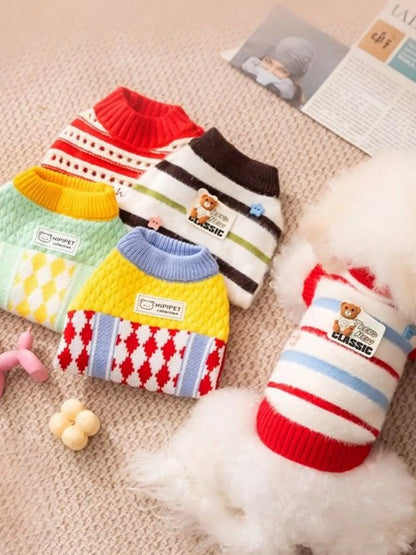 Colorful dog sweaters on a textured surface with a small toy and fur.