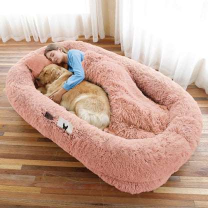 Woman hugging a large pink fluffy dog bed with a golden retriever inside, in a room with curtains.