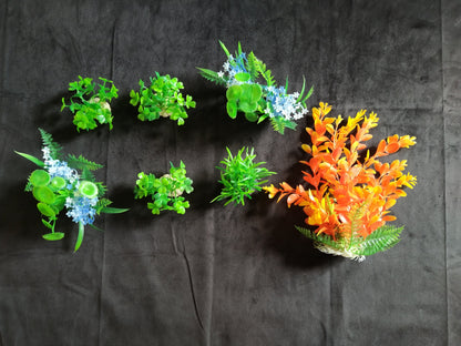 Set of artificial plants and flowers arranged in a circular pattern on a dark fabric background.